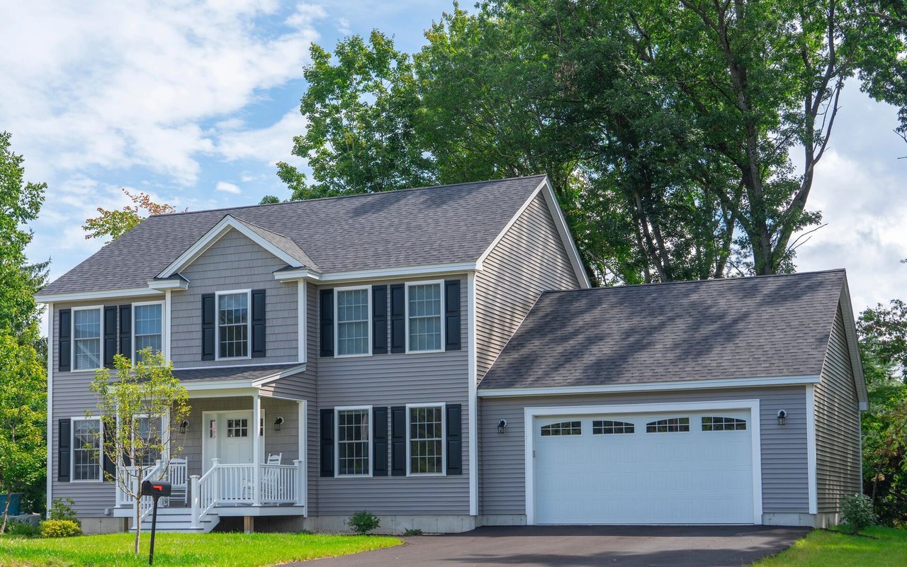 Two-story gray house with a white porch, dark shutters, and an attached two-car garage.