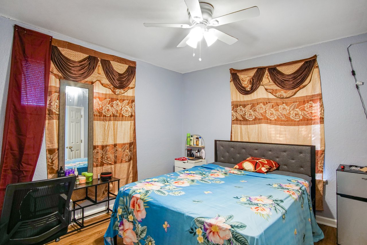 Bedroom at 2506 Nugget Lane in Tallahassee, Florida, featuring light blue walls, wood-look flooring, and a ceiling fan with light fixture. The room is shown with a bed, side table, mirror, and window coverings, offering a functional living space.