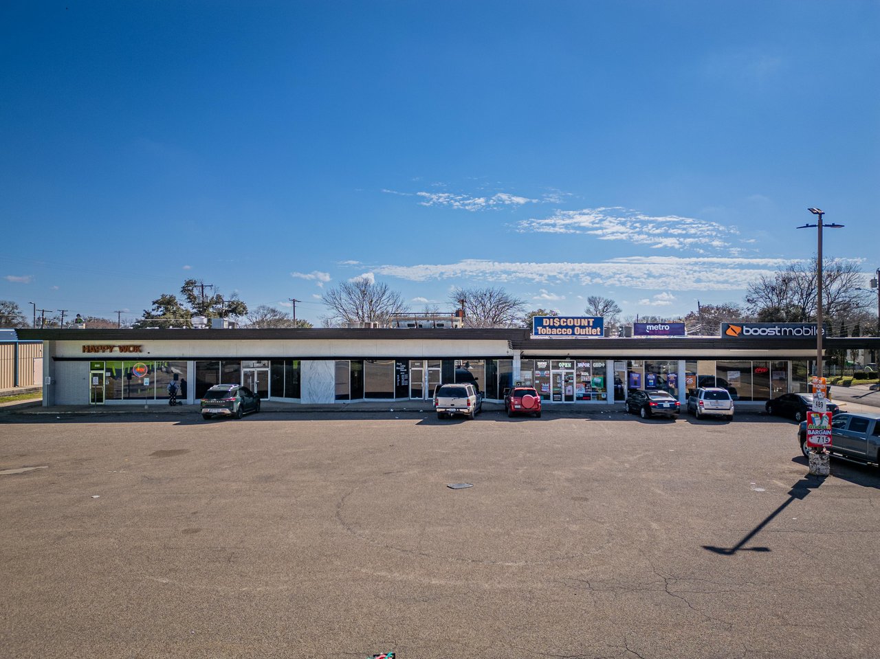 Single-story retail strip center with Discount Tobacco Outlet, Metro, and Boost Mobile storefronts and a large parking lot.