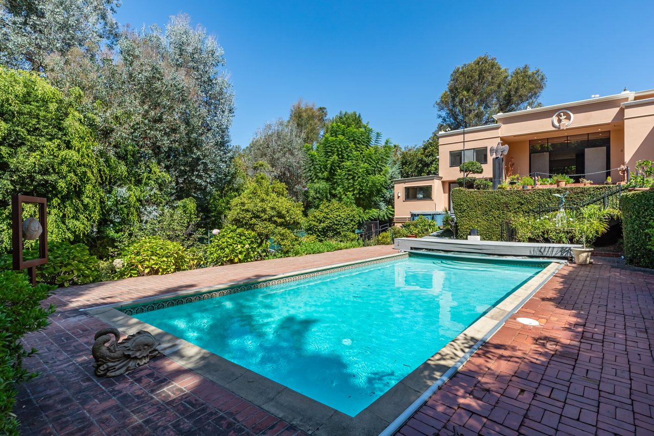 Swimming pool beside a modern residence, with a brick patio and lush garden.
