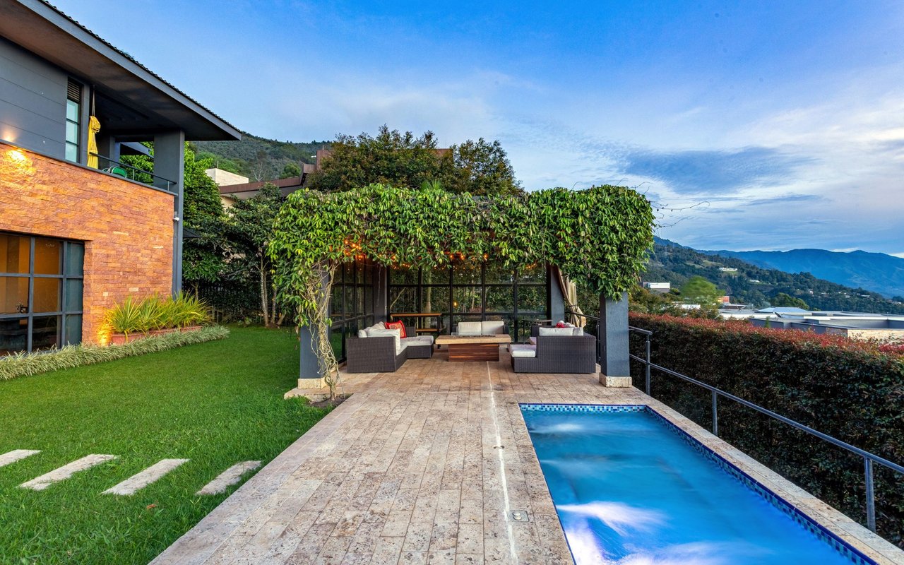Outdoor pool beside a stone patio with a vine-covered pergola and mountain views.