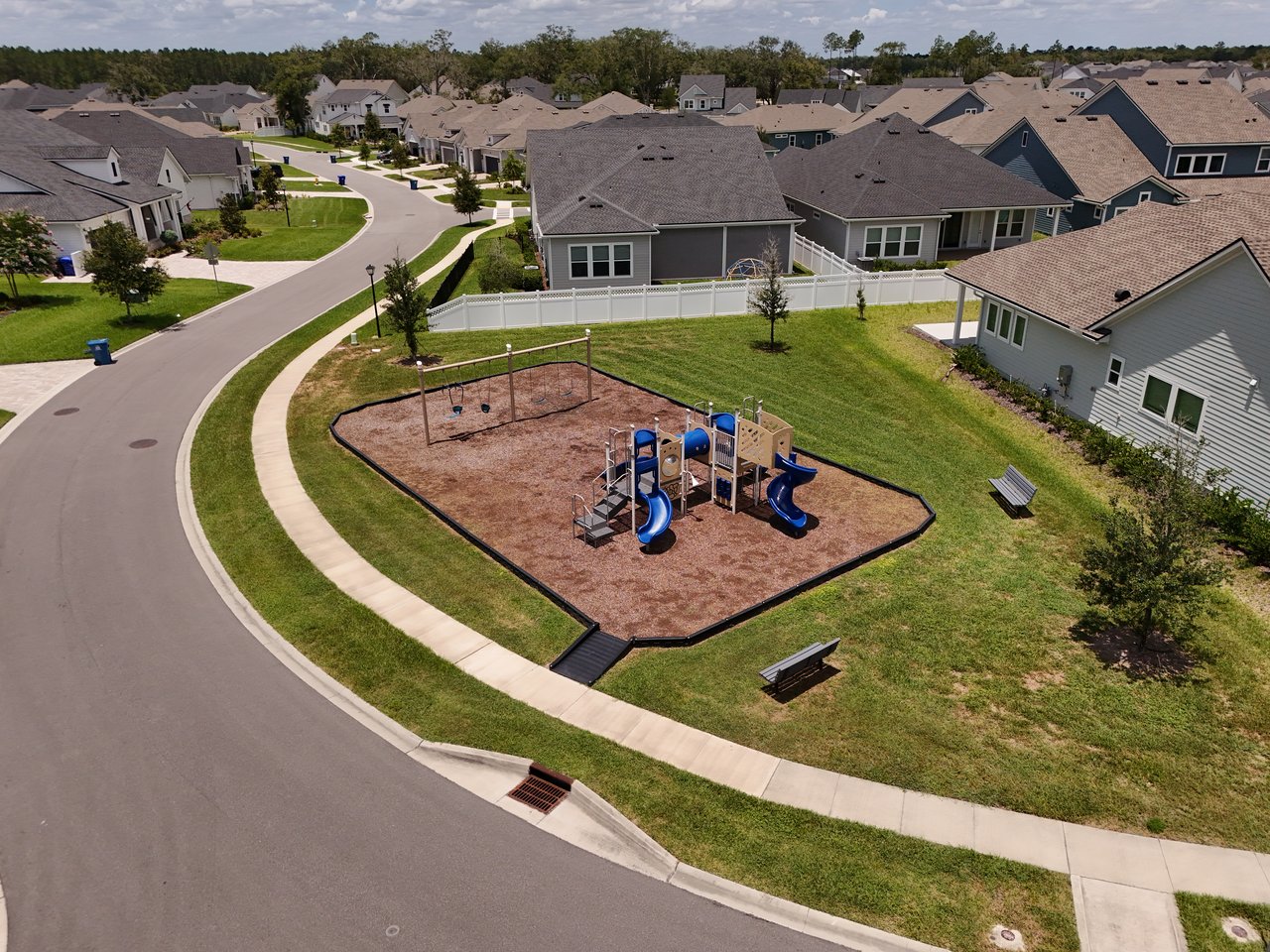 Aerial view of a neighborhood playground surrounded by homes and a curving street.