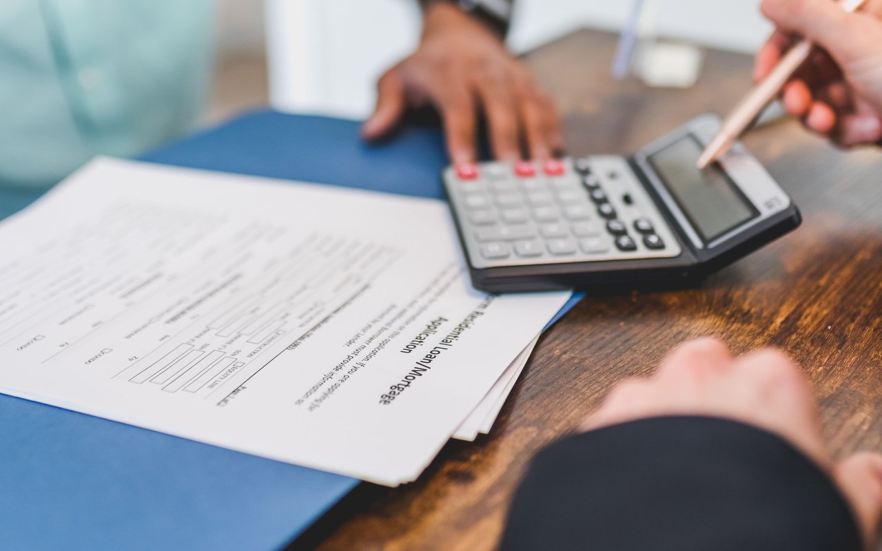 Hands calculate figures beside a residential mortgage application and pen.
