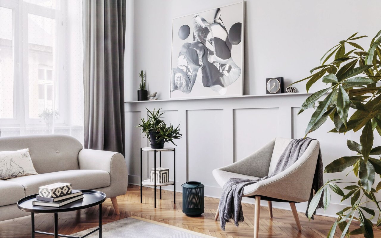 Living room with a gray sofa, armchair, leafy plants, and herringbone wood flooring.