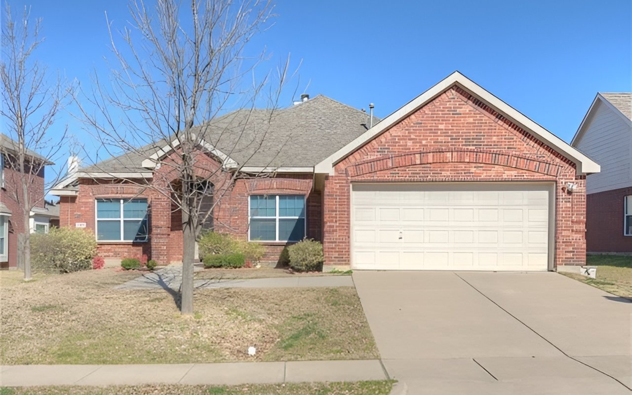 Single-story red brick house with a white double garage door, wide driveway, and leafless front-yard tree.