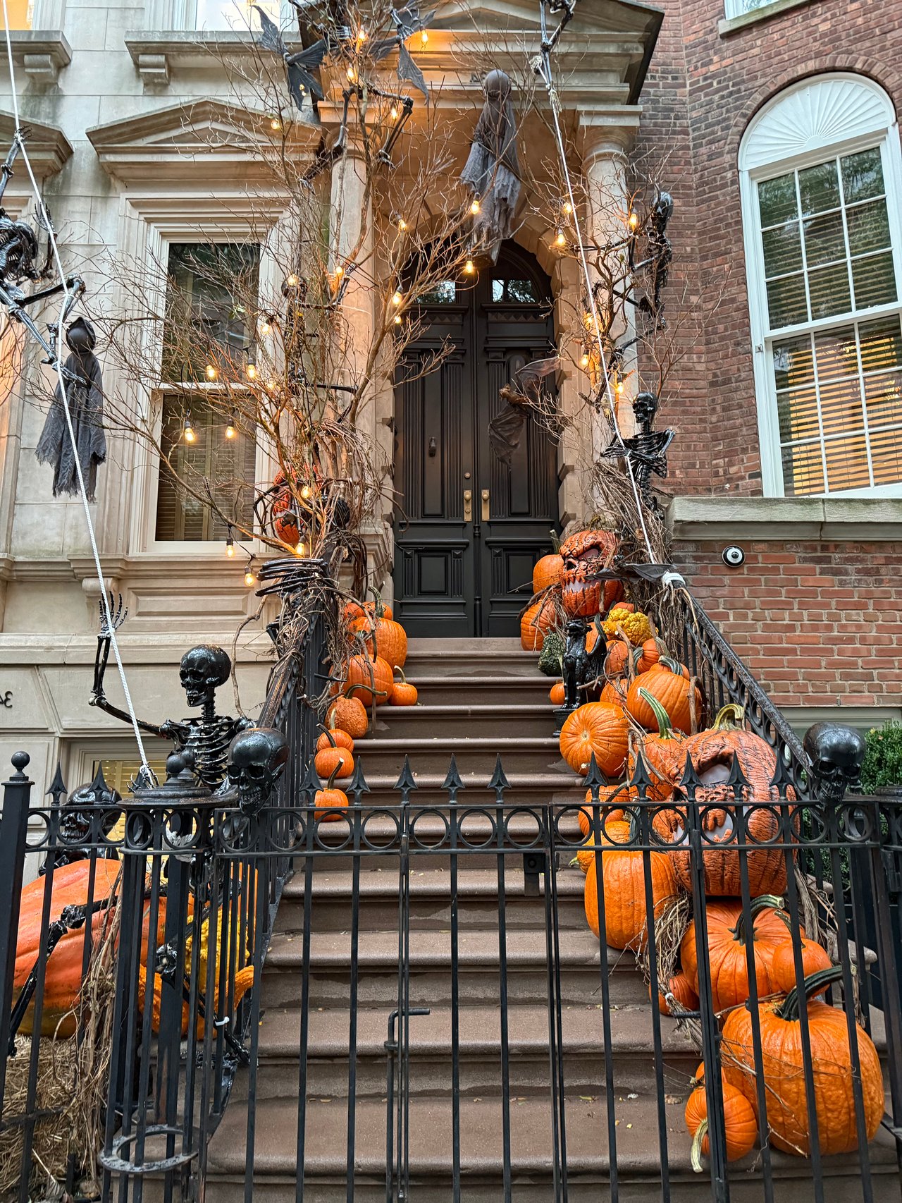 Townhouse entrance decorated with pumpkins, skeletons, and string lights for Halloween.