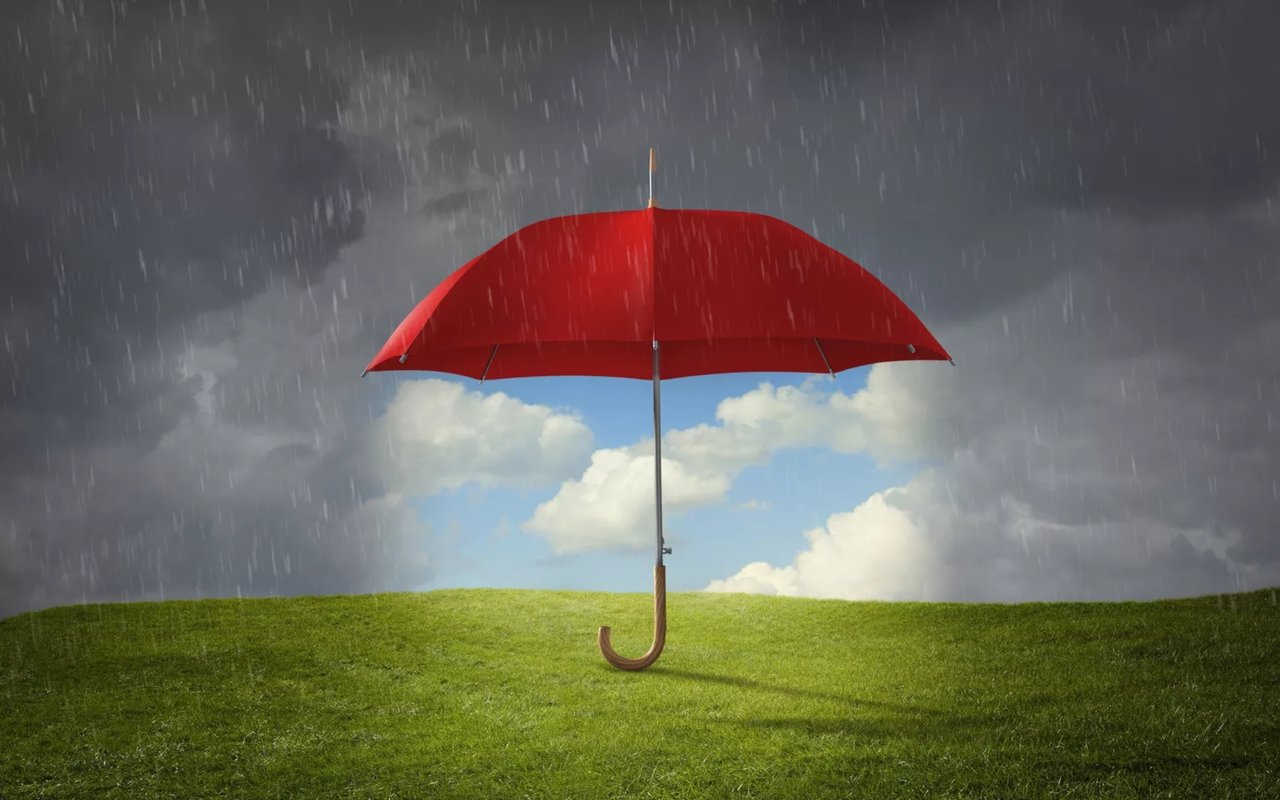Red umbrella shelters a patch of blue sky from rain and dark storm clouds.