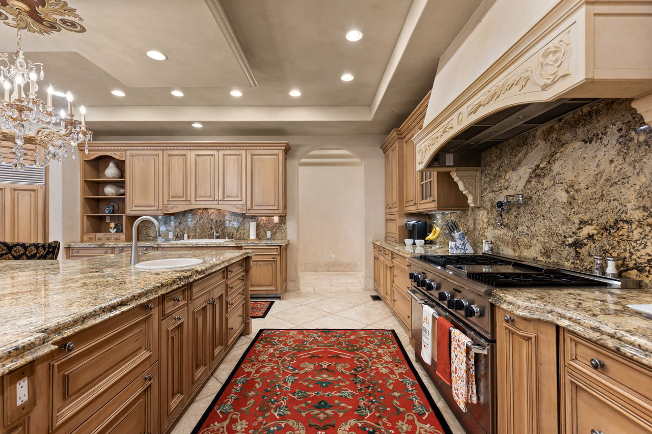 Traditional kitchen with warm wood cabinets, granite counters, and a large range beneath a carved hood.