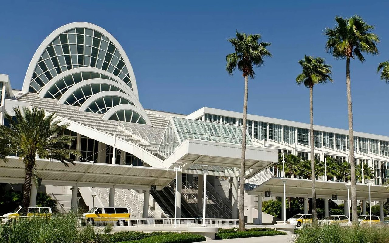 Modern convention center with arched glass roofs and palm trees.