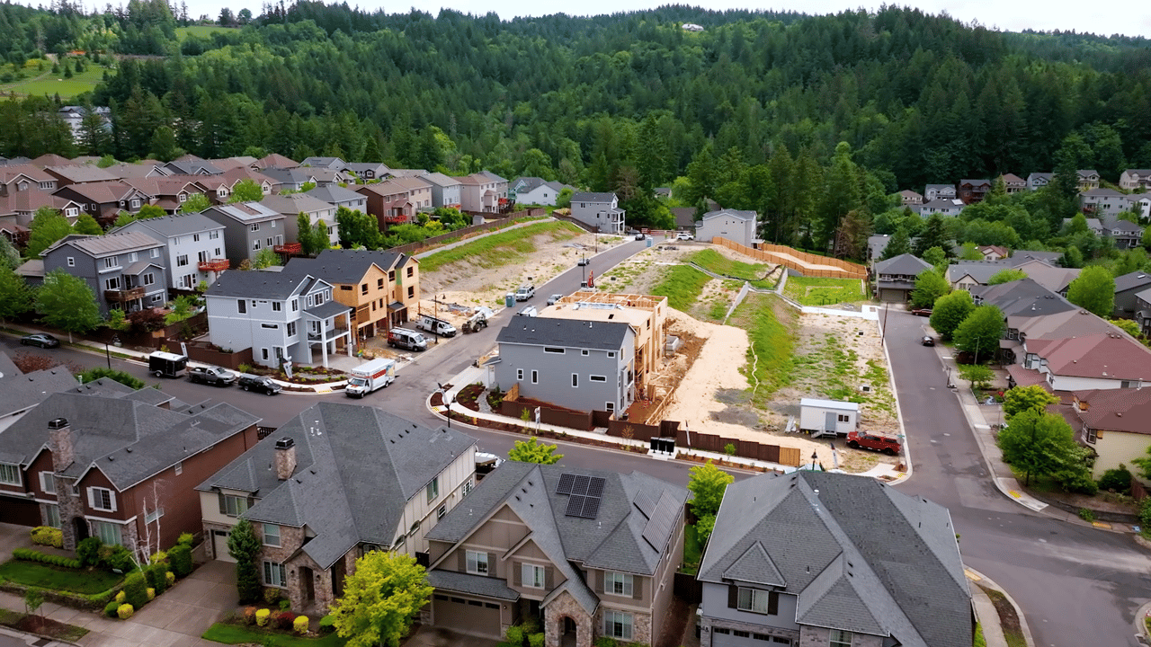 Aerial view of Deer Fern Ridge community in Bethany, Oregon showing ongoing new home construction alongside established houses, nestled in a lush, forested neighborhood.