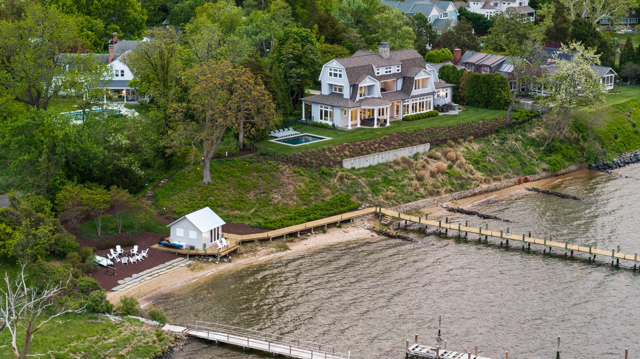 Waterfront home with a pool, long dock, and small beachside outbuilding.