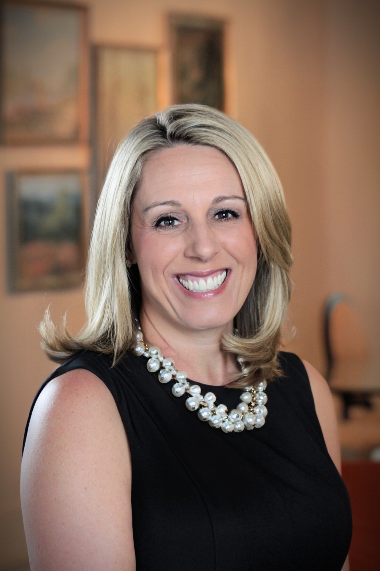 Suzanne Ross smiling in a black sleeveless dress and pearl necklace.