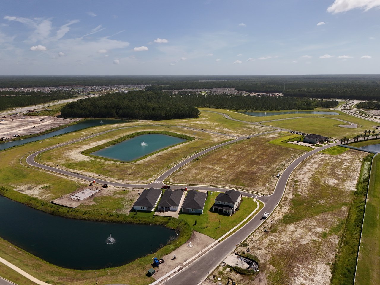 Aerial view of new homes and undeveloped lots surrounding several fountain ponds.