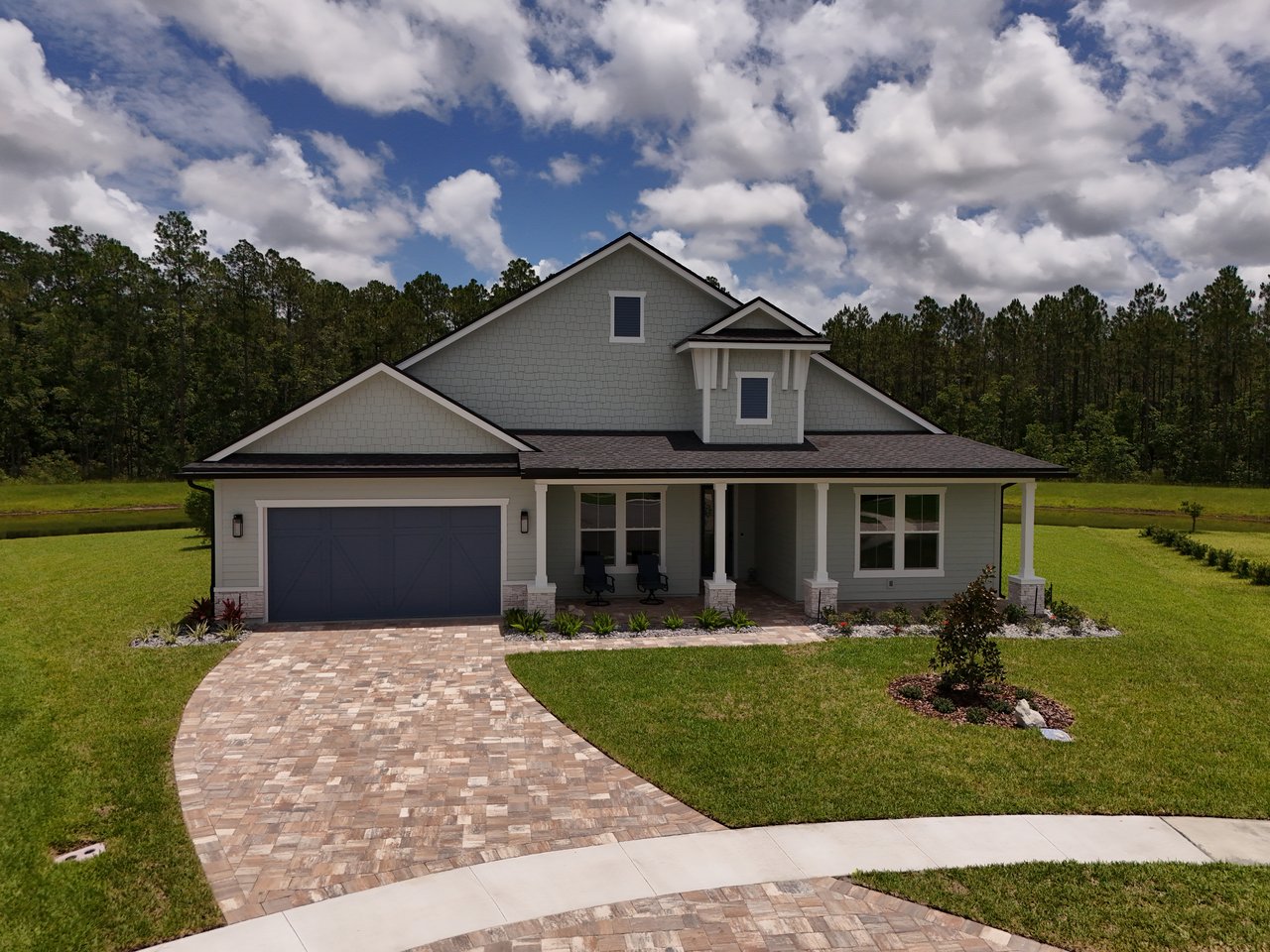 Gray two-story home with a double garage, covered porch, and curved stone-paver driveway.