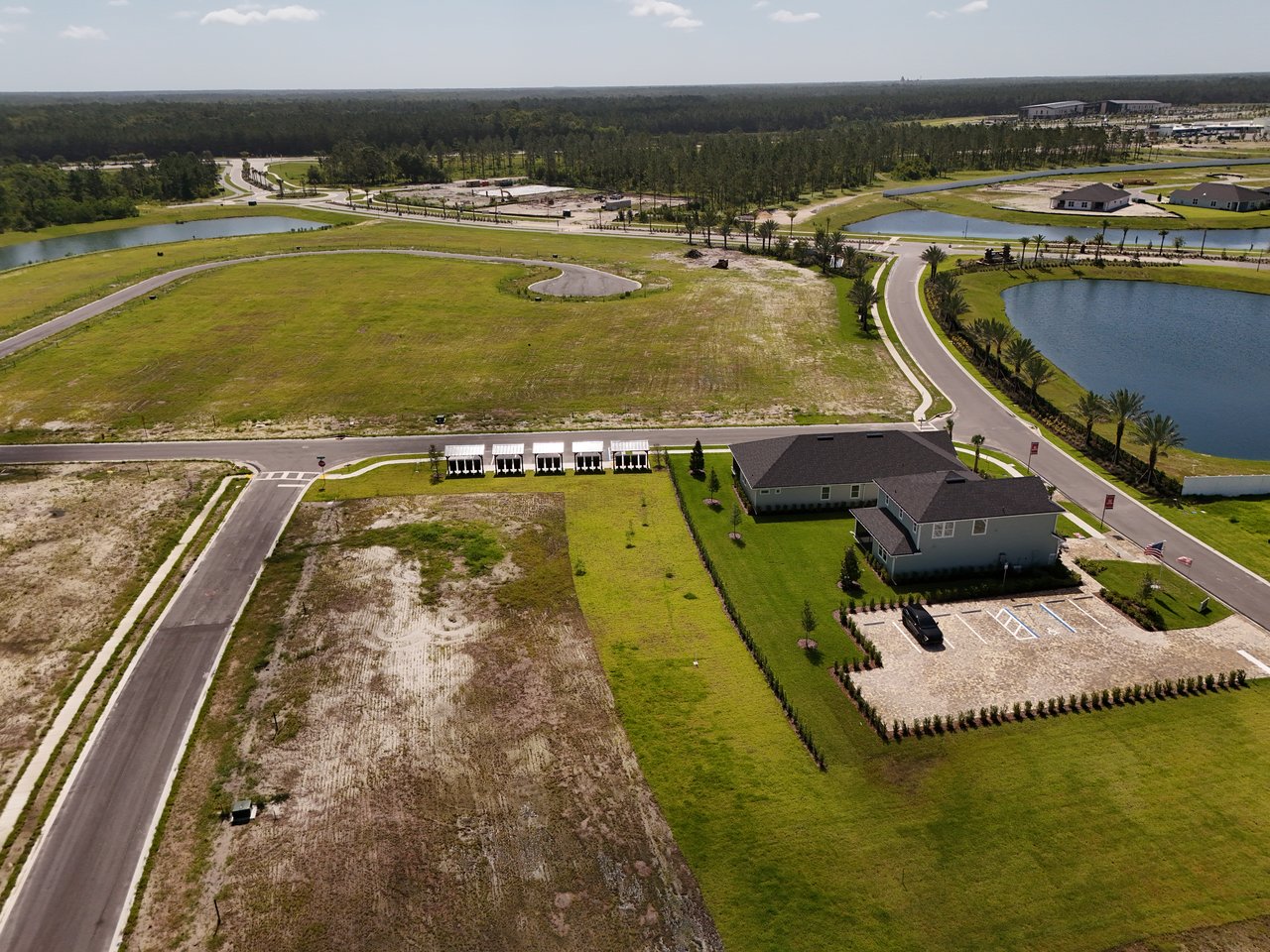 Aerial view of a developing neighborhood with vacant lots, ponds, curving roads, and newly built homes.