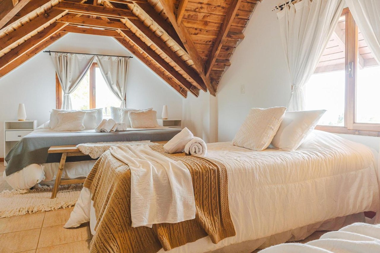 Boutique hotel bedroom with two white beds beneath an exposed timber vaulted ceiling.