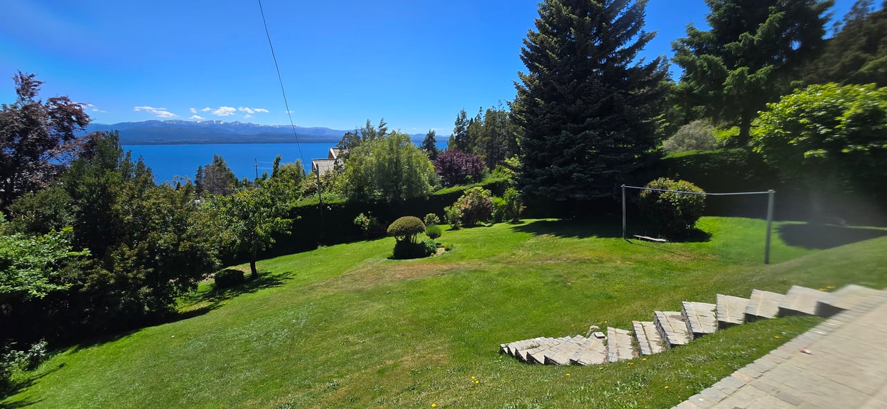 Landscaped garden with stone steps and a volleyball net overlooking a lake and distant mountains.