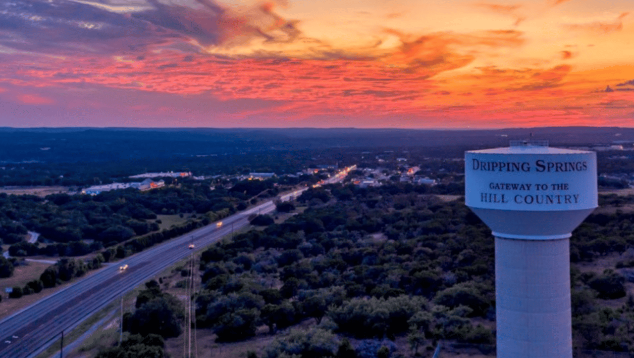 Dripping Springs at dusk, with a highway through wooded hills and a water tower reading “Gateway to the Hill Country.”