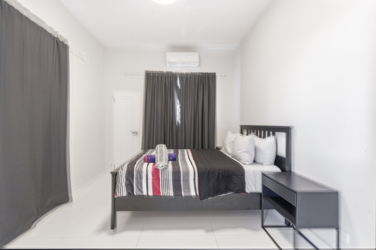 Furnished bedroom with a dark bed, striped bedding, gray curtains, and a wall-mounted air conditioner.