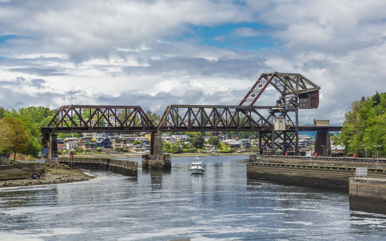 Ballard railroad bridge over the water, with a boat passing beneath and homes along the shore.