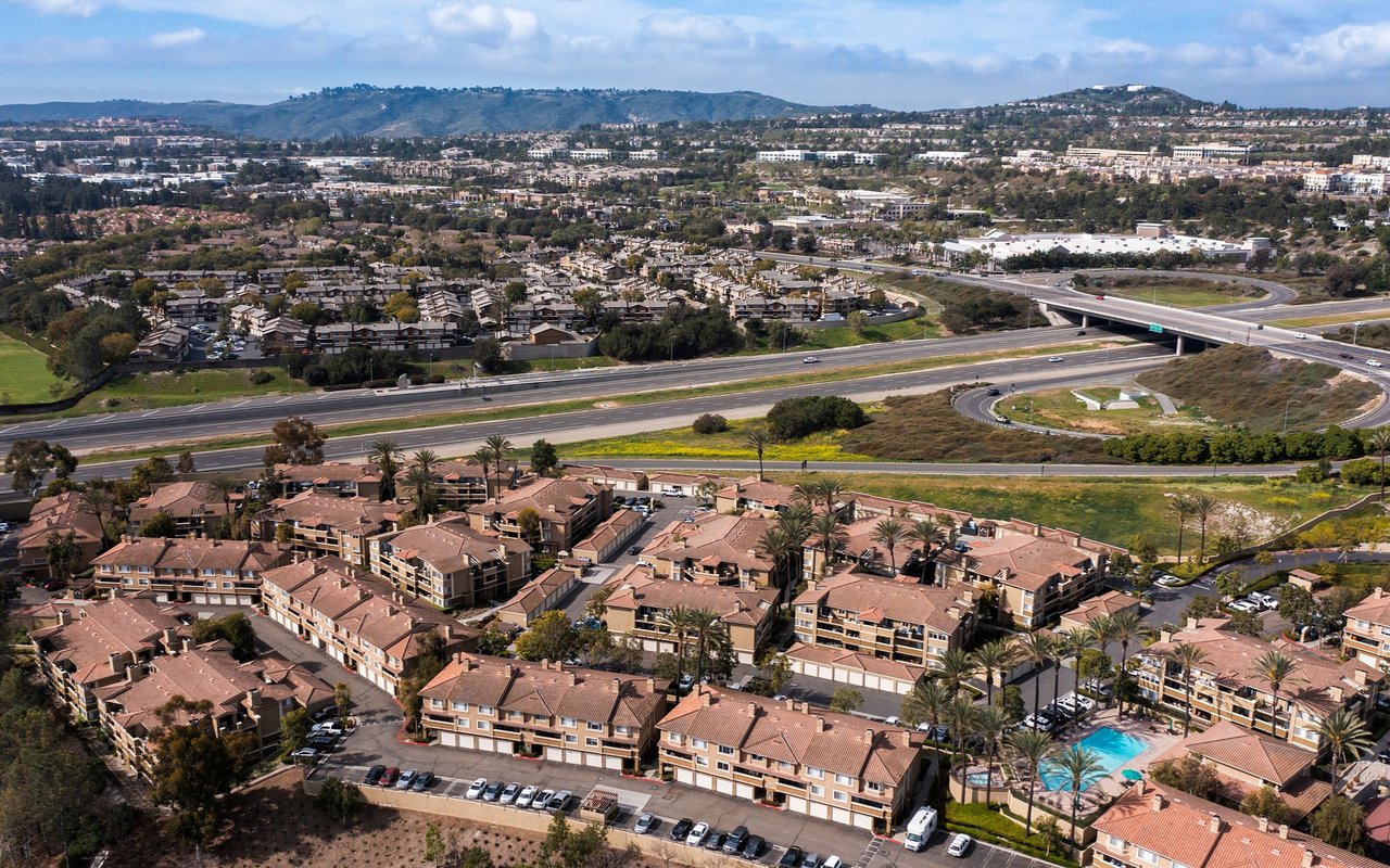 Aerial view of Aliso Viejo apartments, with a swimming pool, highway interchange, and distant hills.