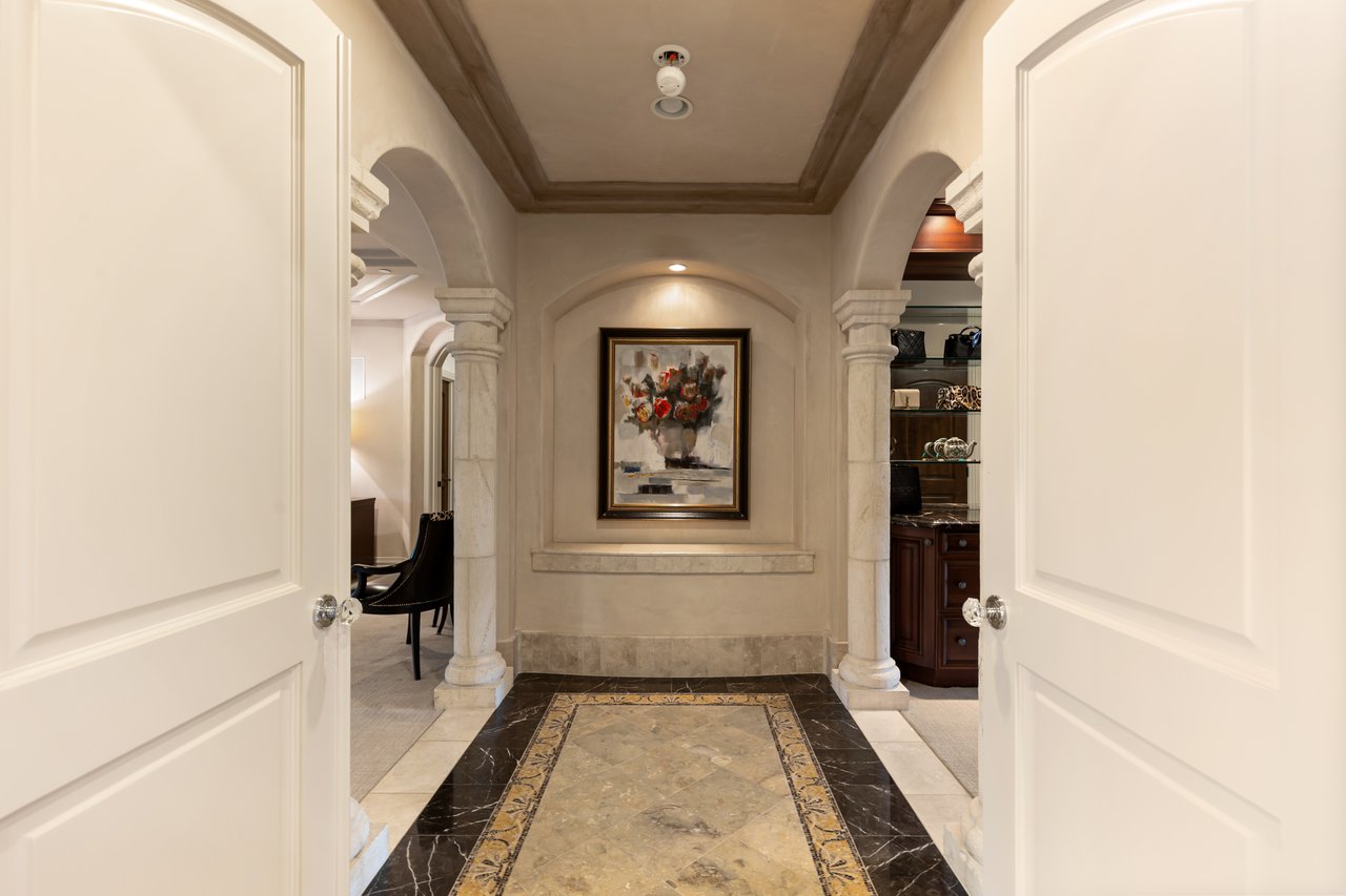 Entry hall with stone arches, a floral painting, and a decorative marble floor.