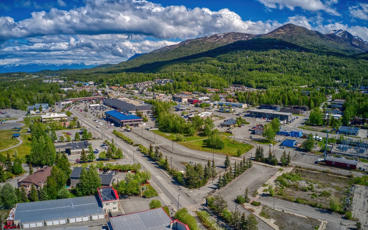 Aerial view of a town beneath forested mountains and a partly cloudy sky.