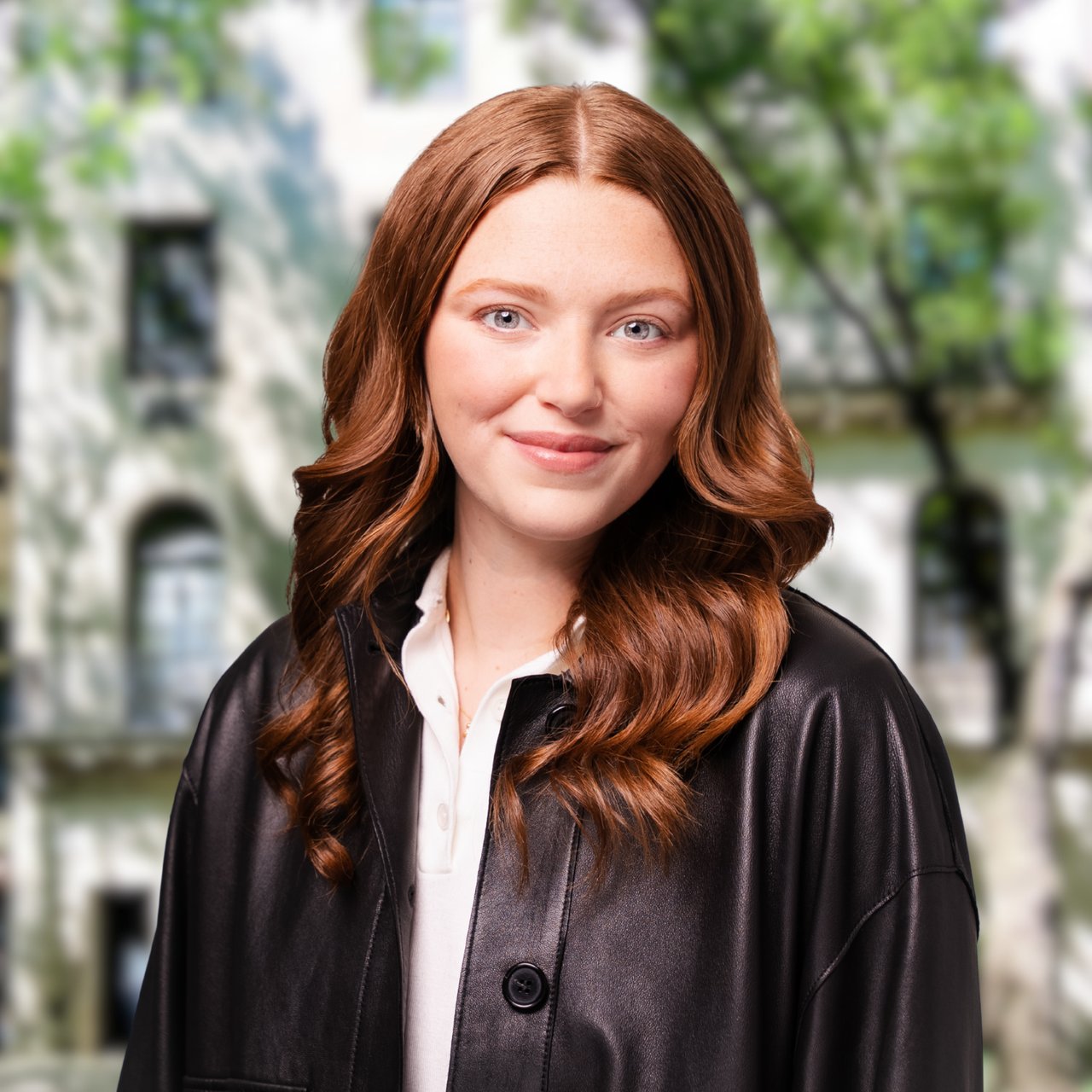 Bar Tidhar with long auburn hair, wearing a black leather jacket over a white top