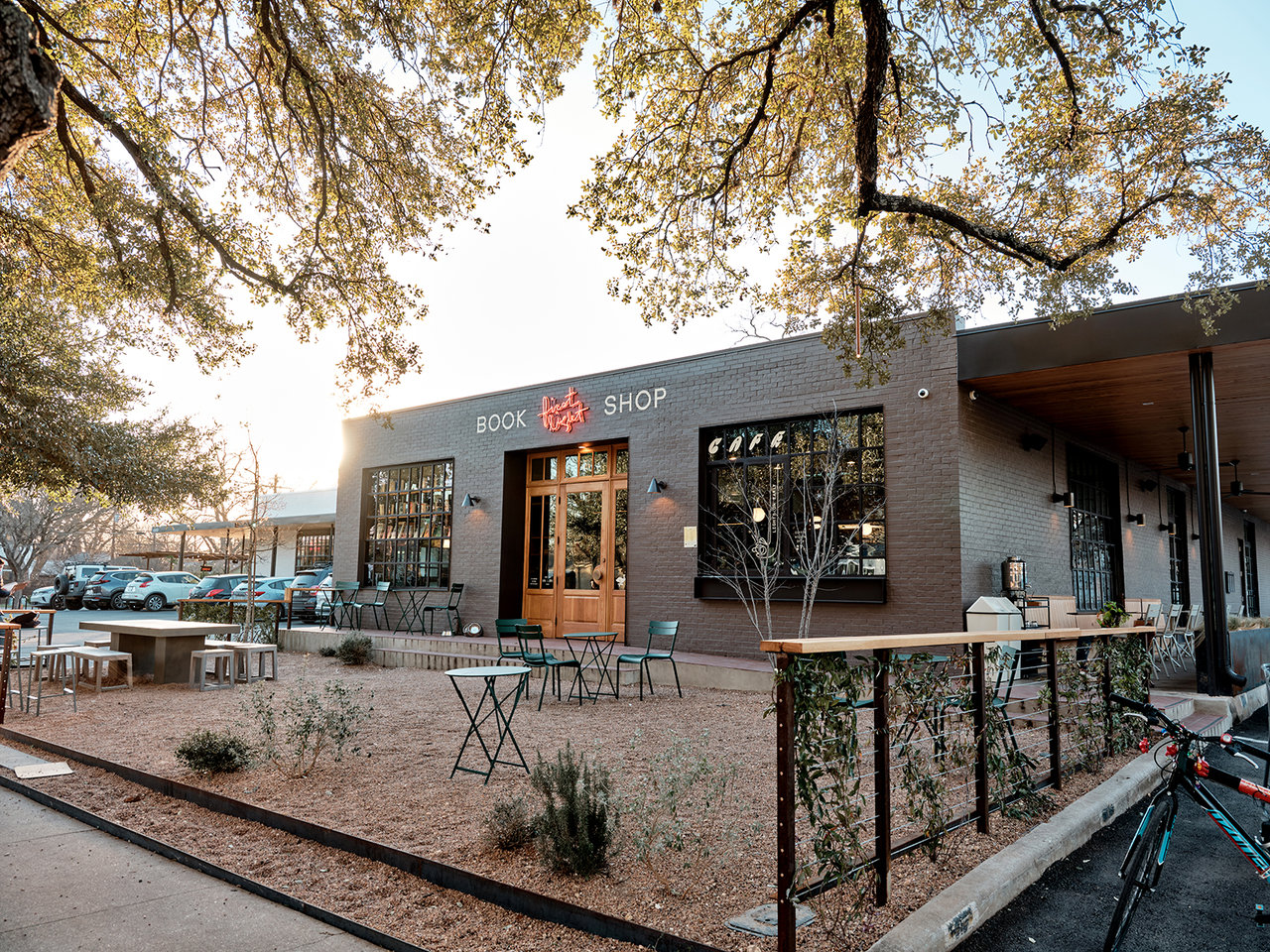 Neighborhood bookshop with large windows, outdoor seating, and mature trees in golden-hour light.