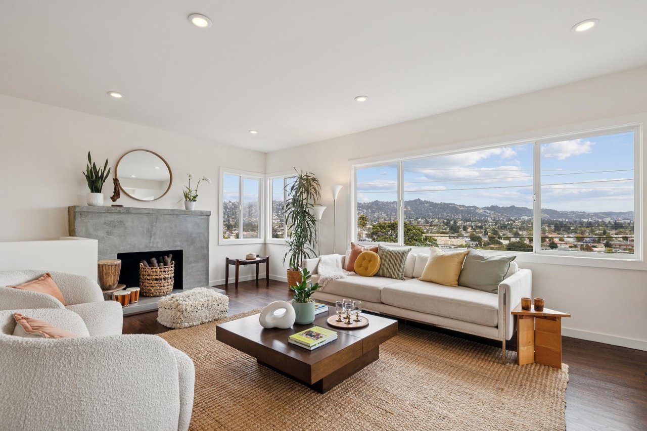 Living room with a concrete fireplace, cream sofas, and wide windows overlooking the city and hills.
