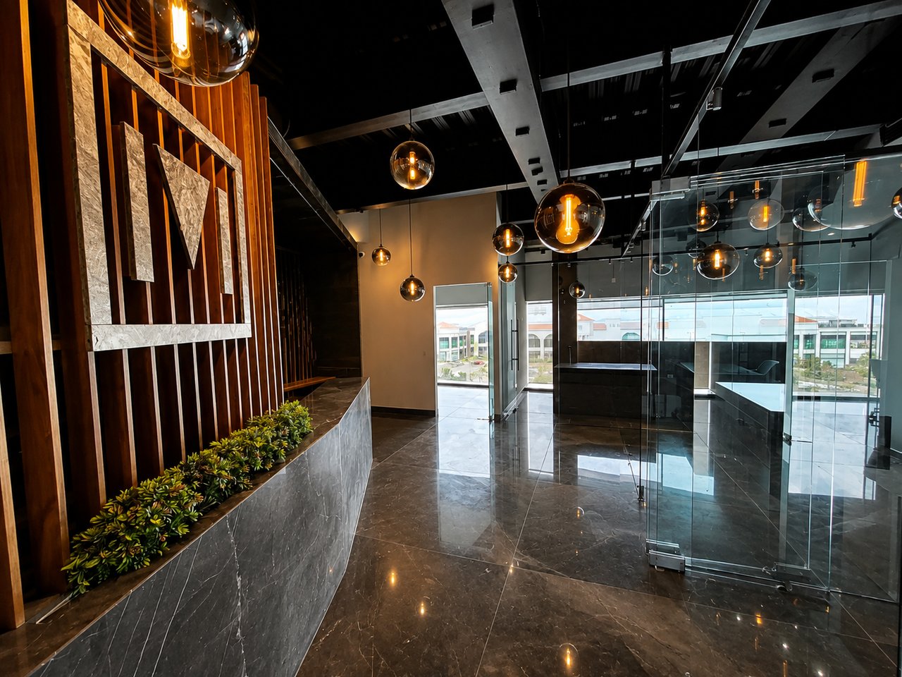 Corporate office lobby with a marble reception counter, amber pendant lights, and glass-walled offices.