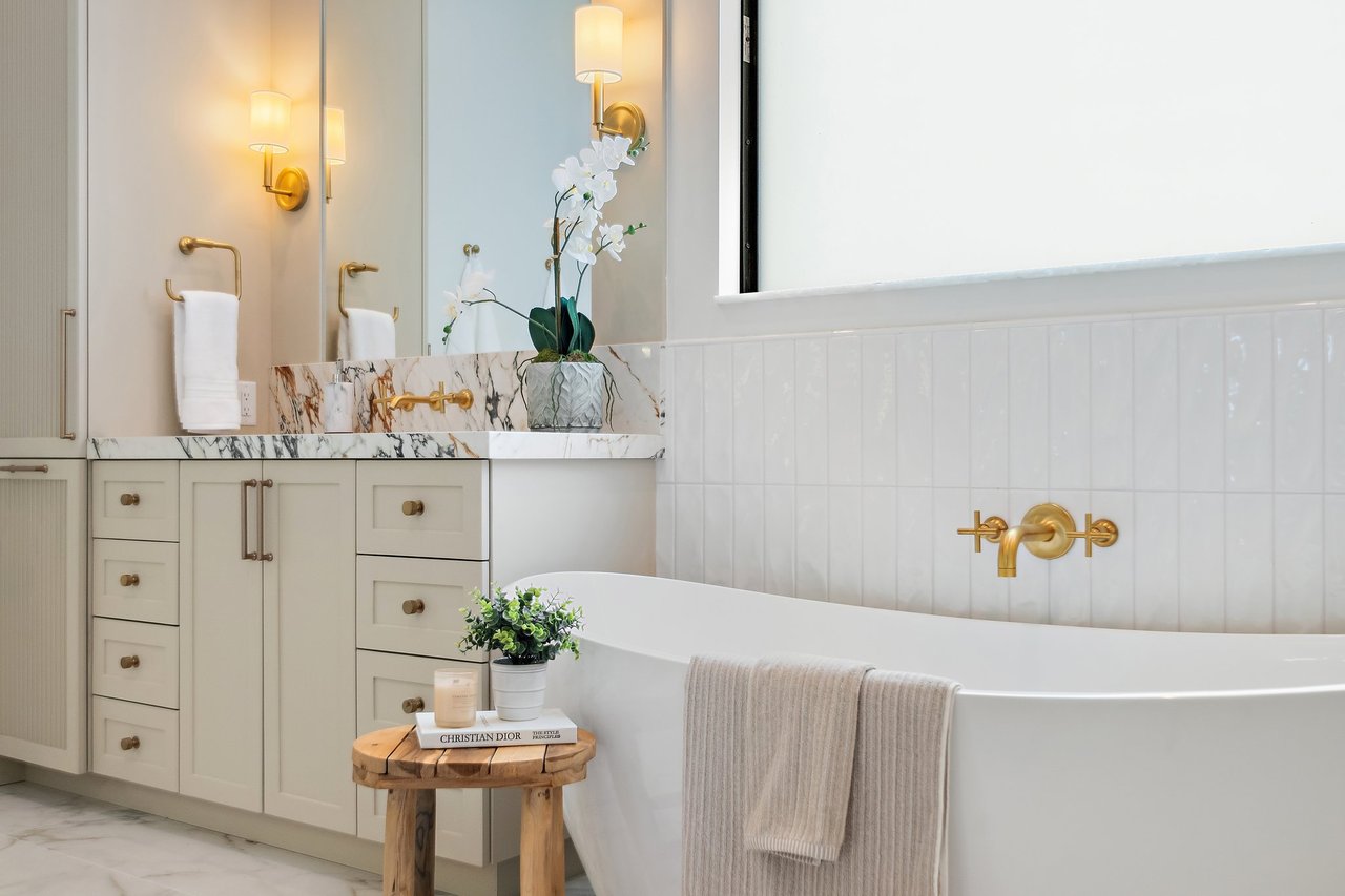 Bathroom with a freestanding tub, gold fixtures, marble vanity, and white orchids.