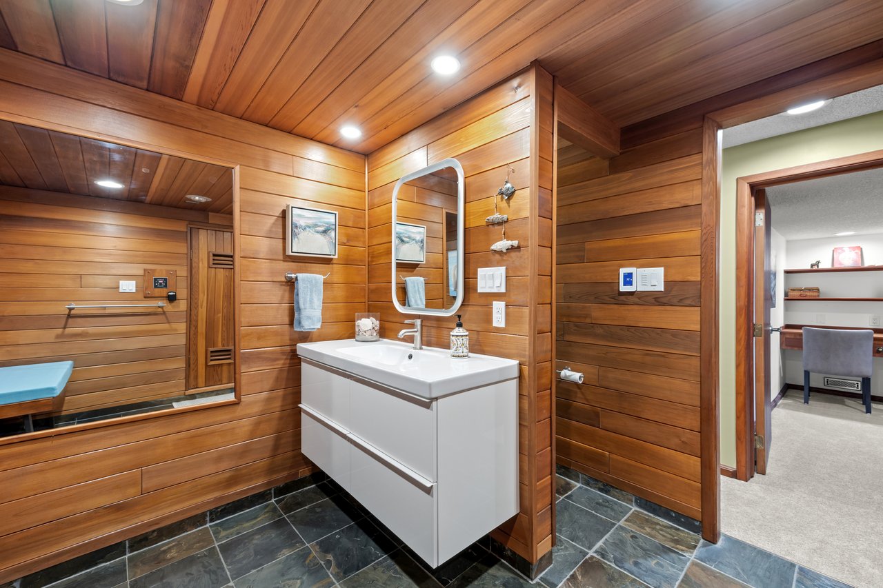 Wood-paneled bathroom with a floating white vanity, large mirror, and dark tile floor.