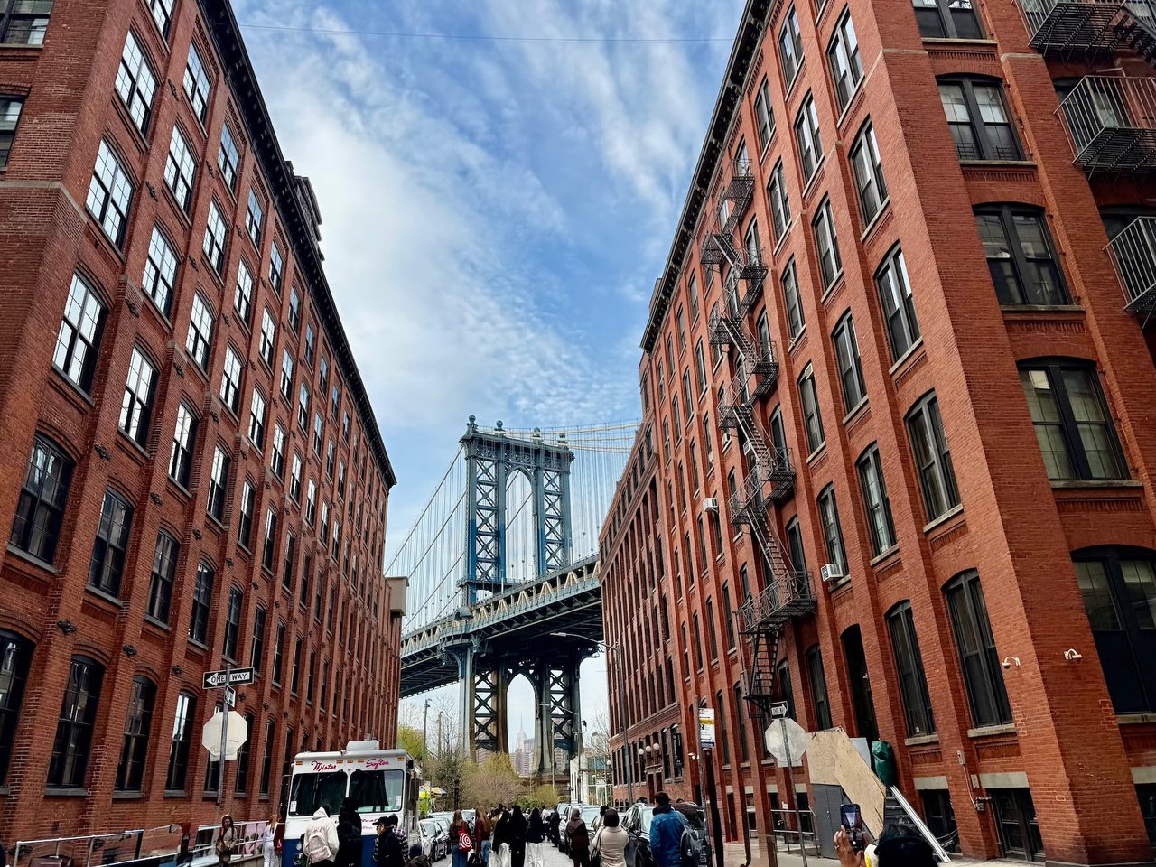 Manhattan Bridge framed by red-brick buildings on a busy New York City street.
