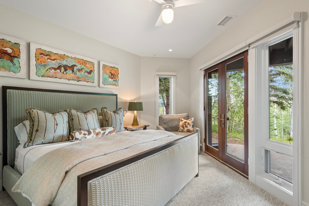 Bedroom with an upholstered bed and wood-framed glass doors overlooking trees.