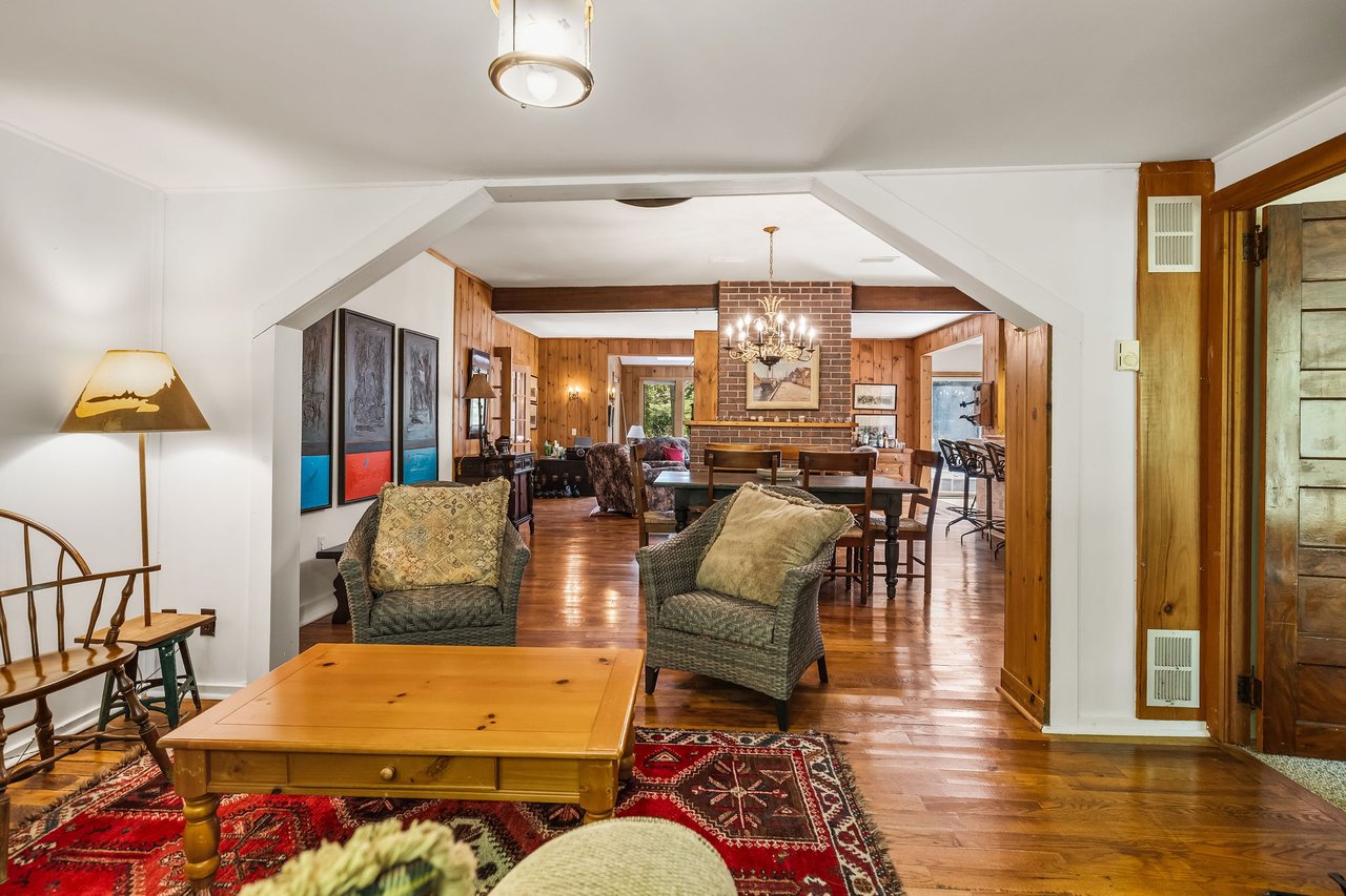 Living and dining area with wood-paneled walls, brick fireplace, and hardwood floors.