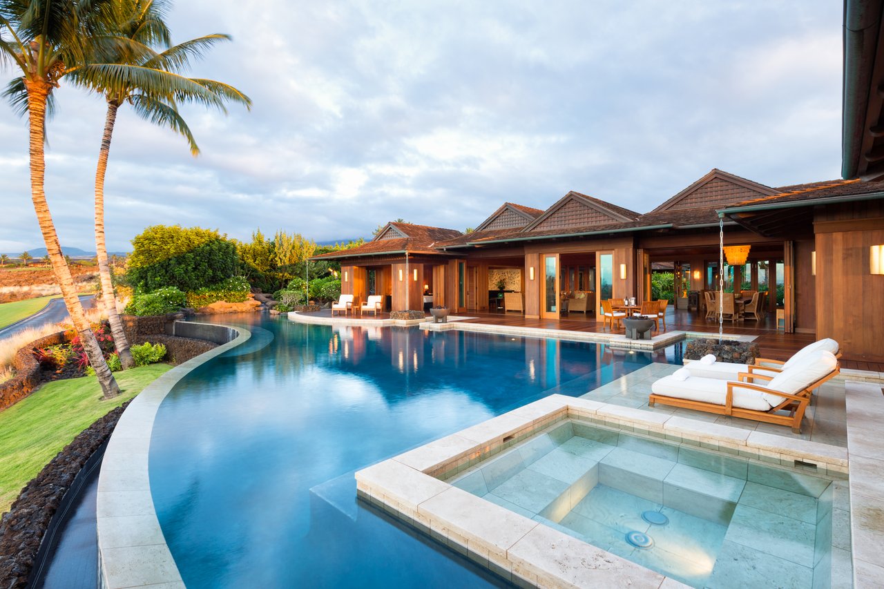 Tropical home beside a curved pool and square spa, with palm trees and outdoor loungers.