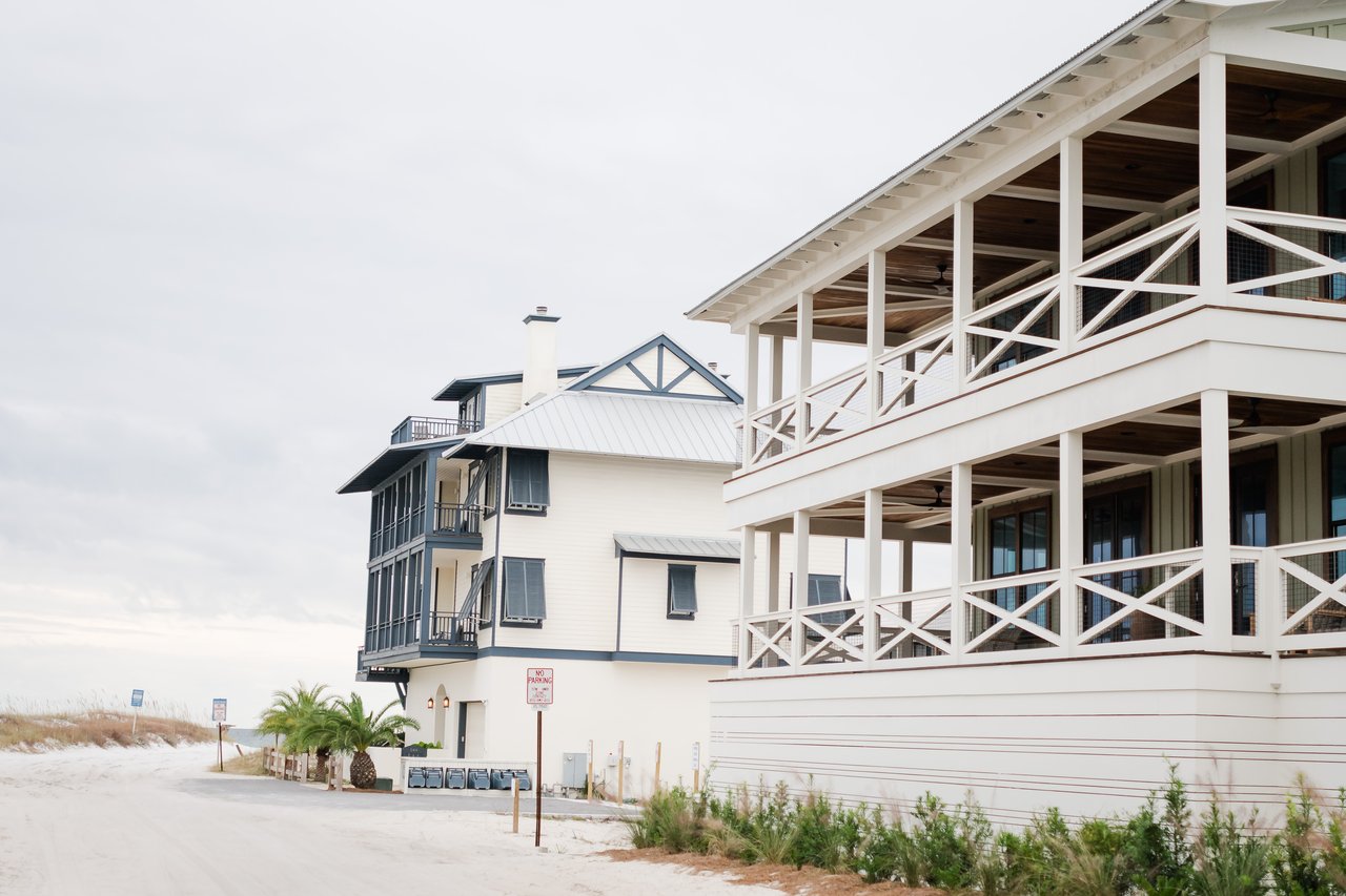 Weathered white two-story cottage with wraparound porches and a silver metal roof at the sandy edge of Grayton Beach on 30A, Florida