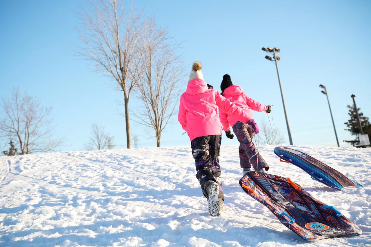 Two people pull colorful sleds uphill through snow.