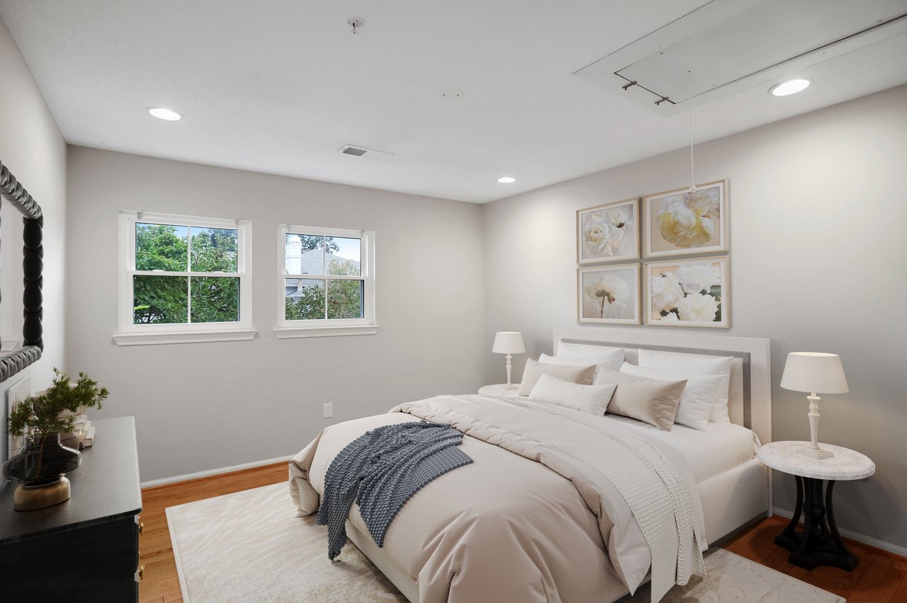 Staged bedroom with a white bed, blue knitted throw, two windows, and floral artwork above the headboard.