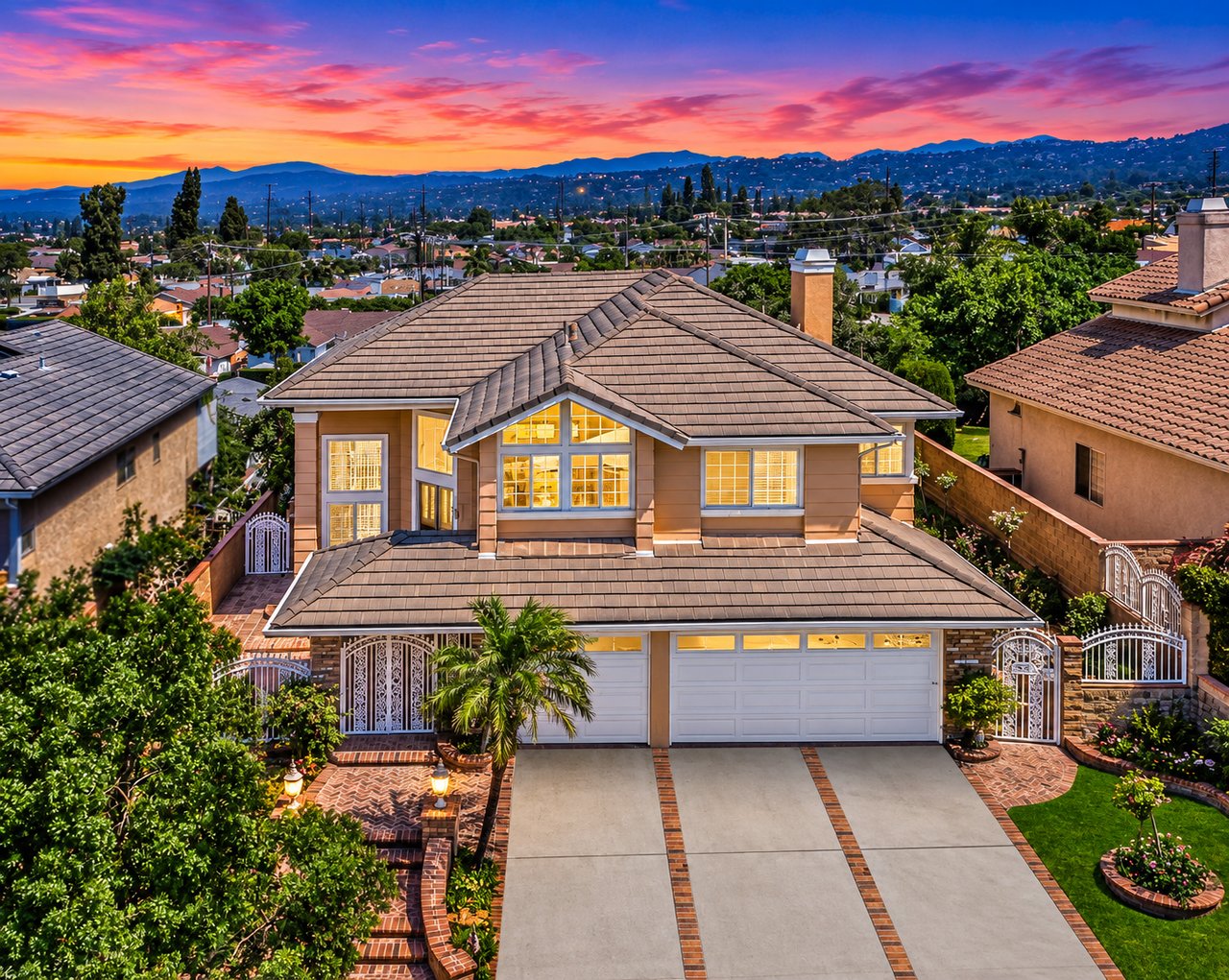 Two-story home with a tiled roof and landscaped driveway beneath a vivid sunset sky.