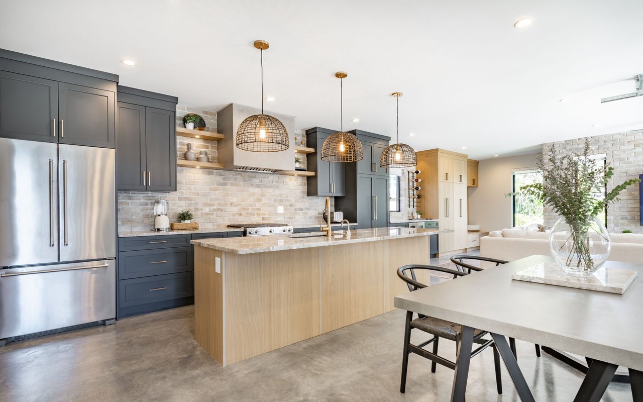 Open-plan kitchen with charcoal cabinets, stainless steel appliances, and a wood-paneled island.