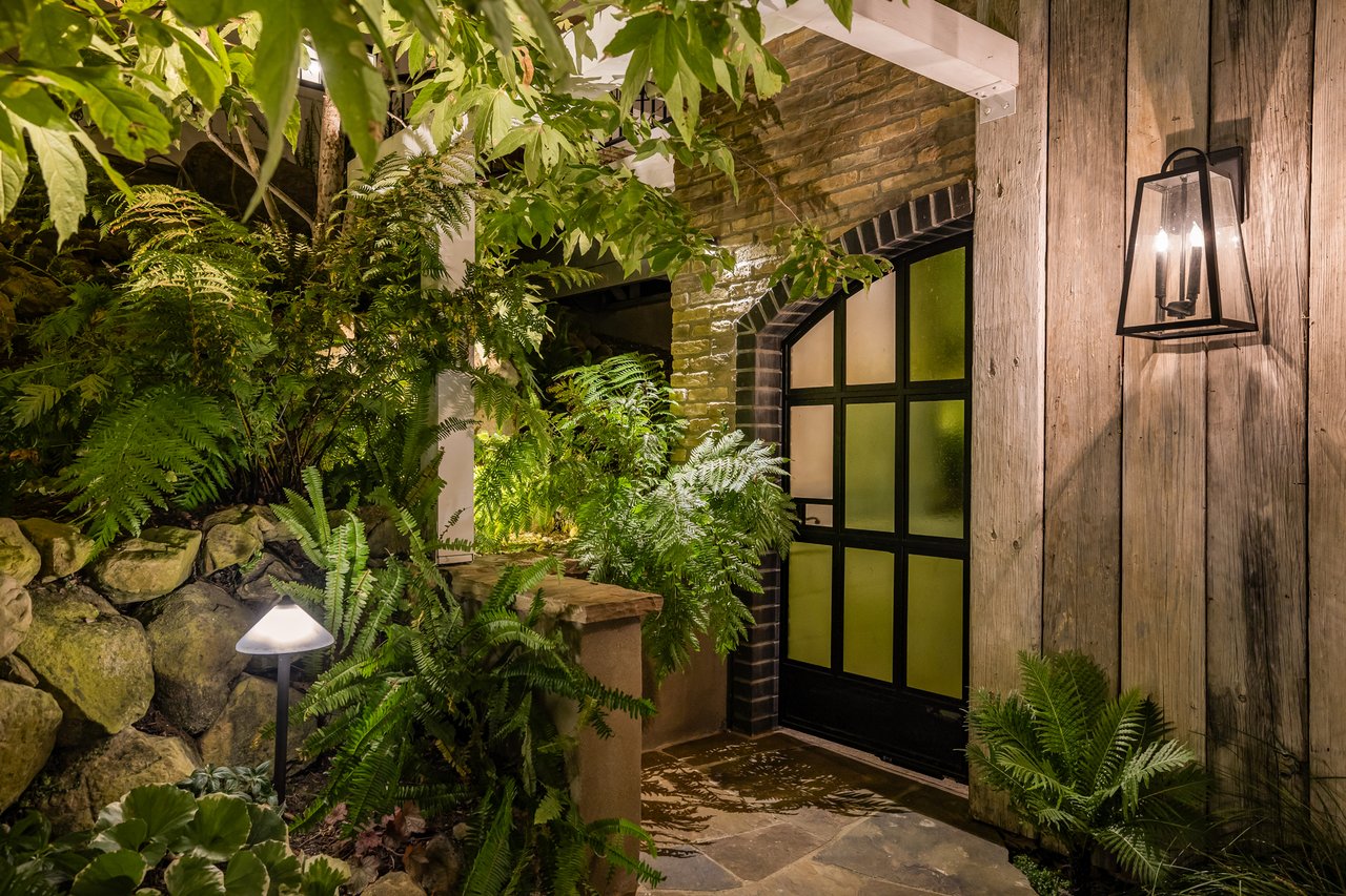 Home entrance with a black divided-light door, brick arch, ferns, and warm lantern lighting.