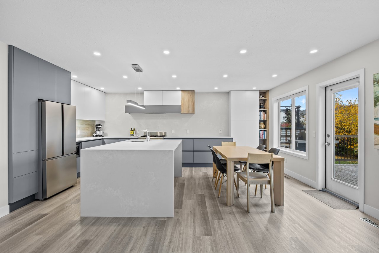 Modern kitchen with a large white island, gray cabinetry, and dining table beside a deck door.