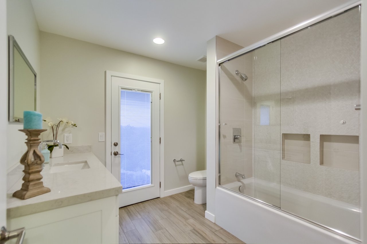 Bathroom with glass-enclosed tub and shower, white vanity, and wood-look tile flooring.
