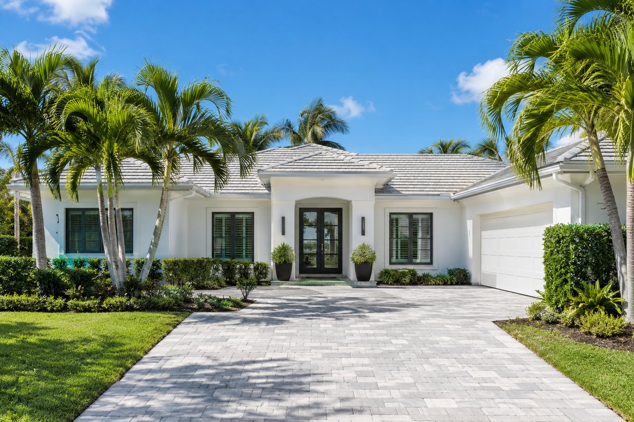 White single-story home with a gray tile roof, palm trees and a paver driveway in Jupiter, Florida, ready to sell this winter