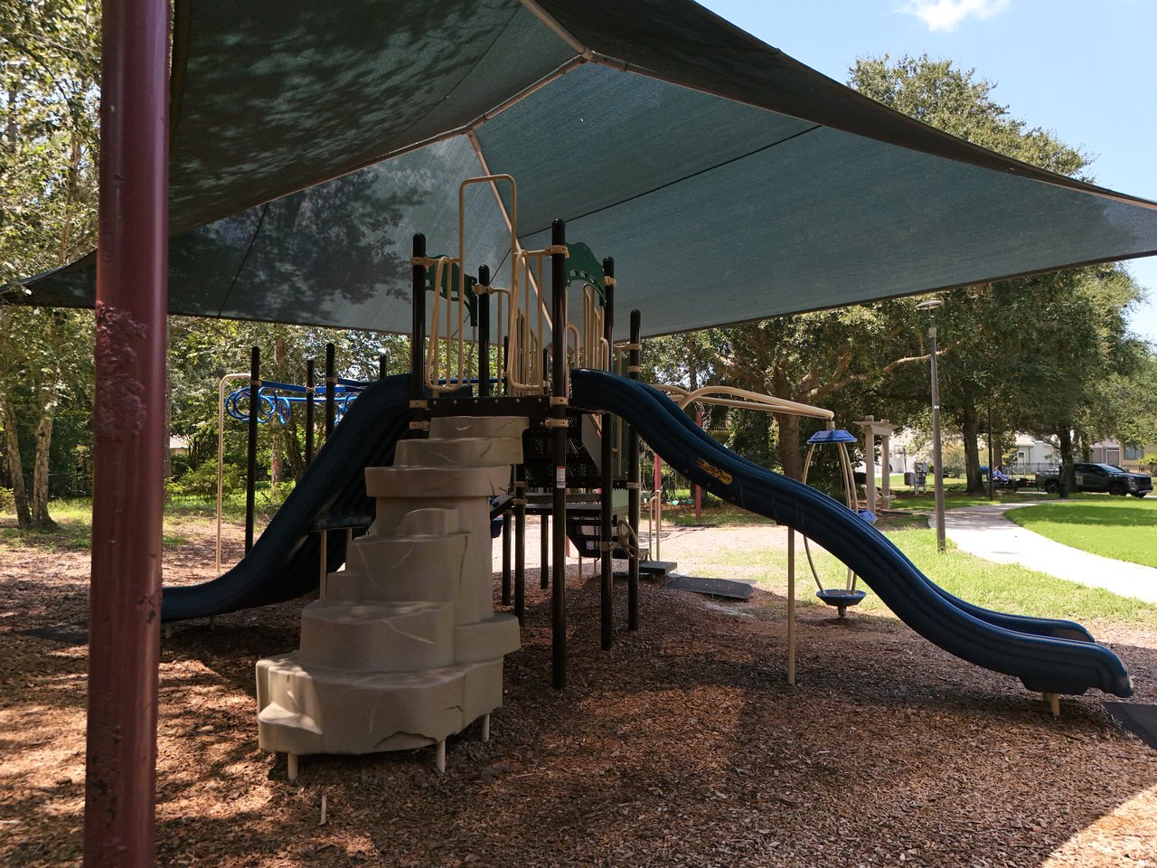 Community playground with a shaded climbing structure and two long blue slides