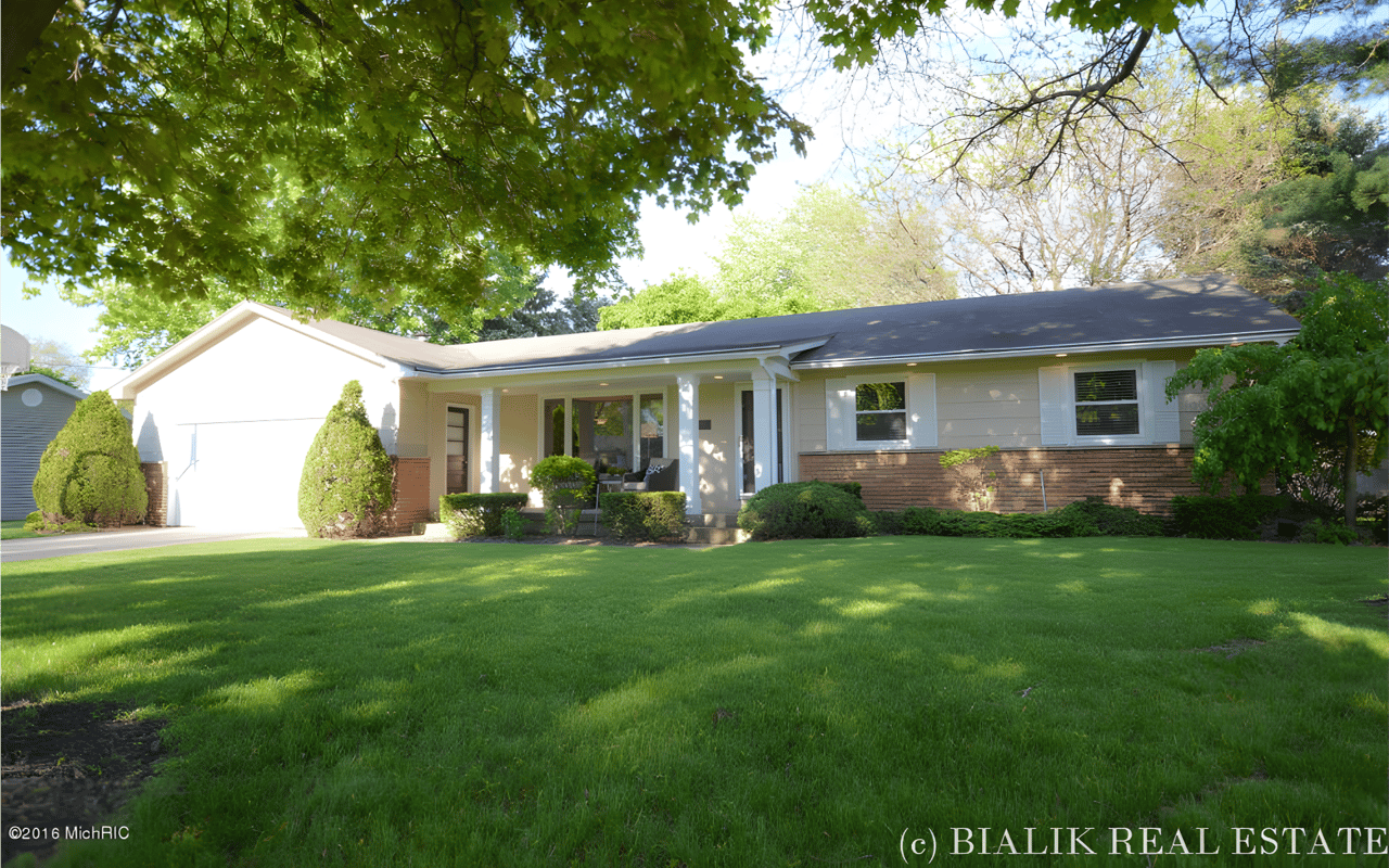 Single-story home with a broad lawn, mature trees, and a covered front porch.