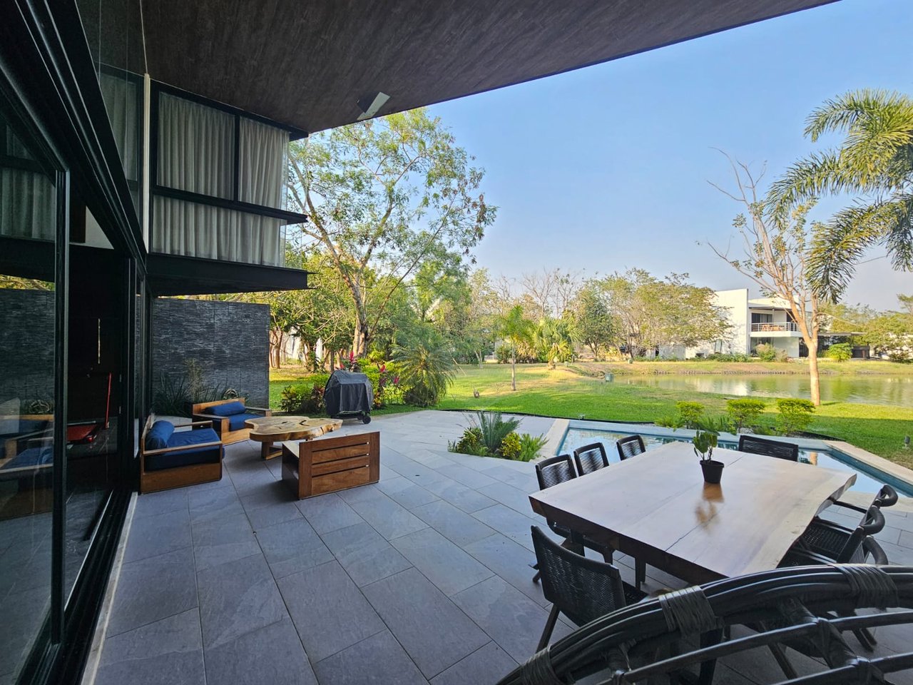Modern home's furnished patio with dining area, pool, and landscaped lakefront view.