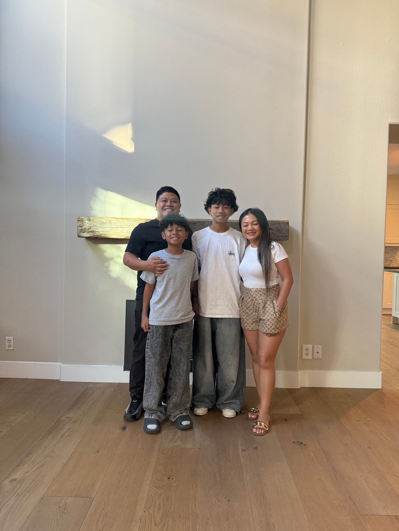 Family of four posing together in a home in front of a wooden mantel.